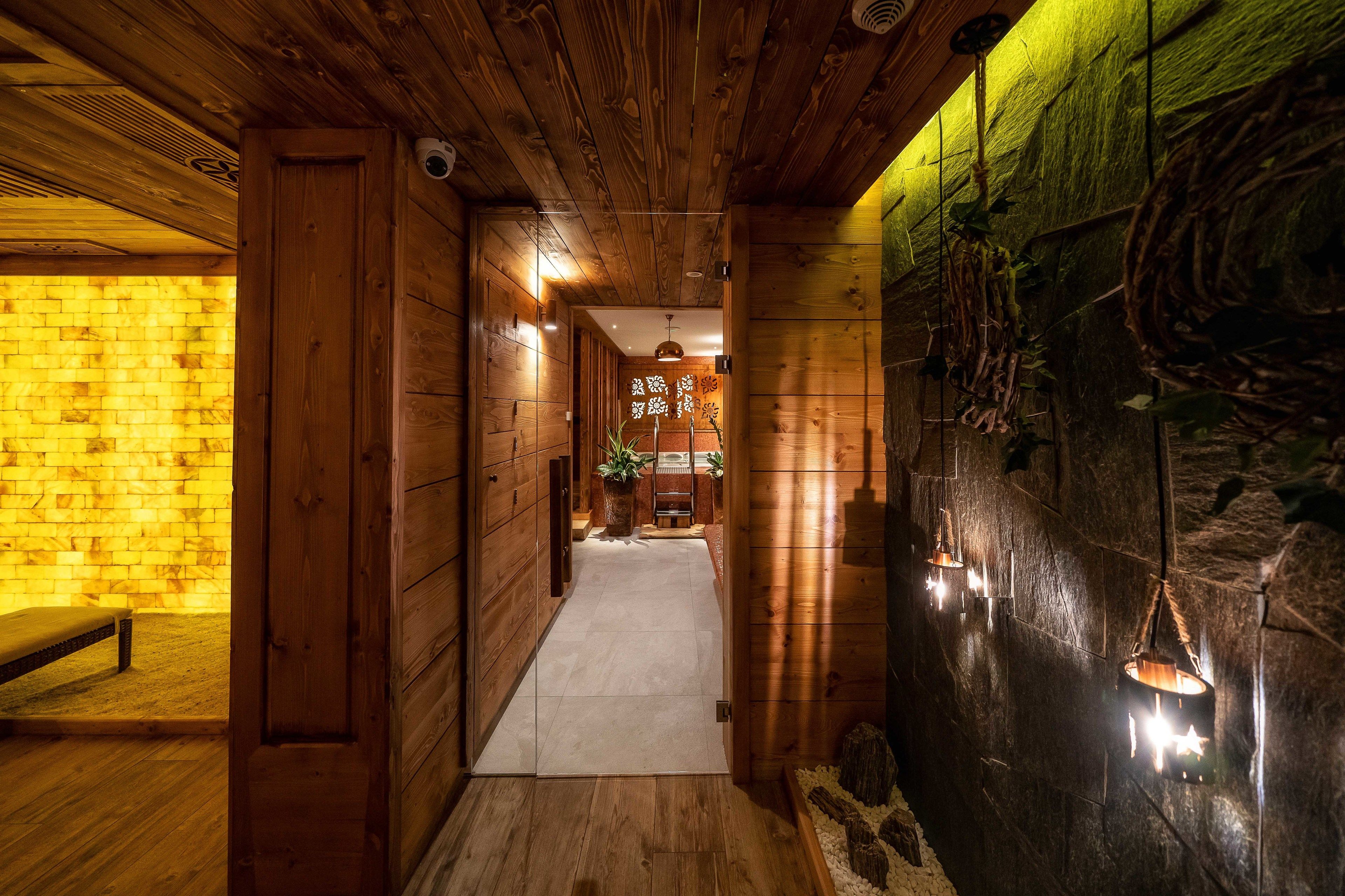 Een houten interieurhal met een bank, een betegelde vloer en een stenen muur met hangende lampen.