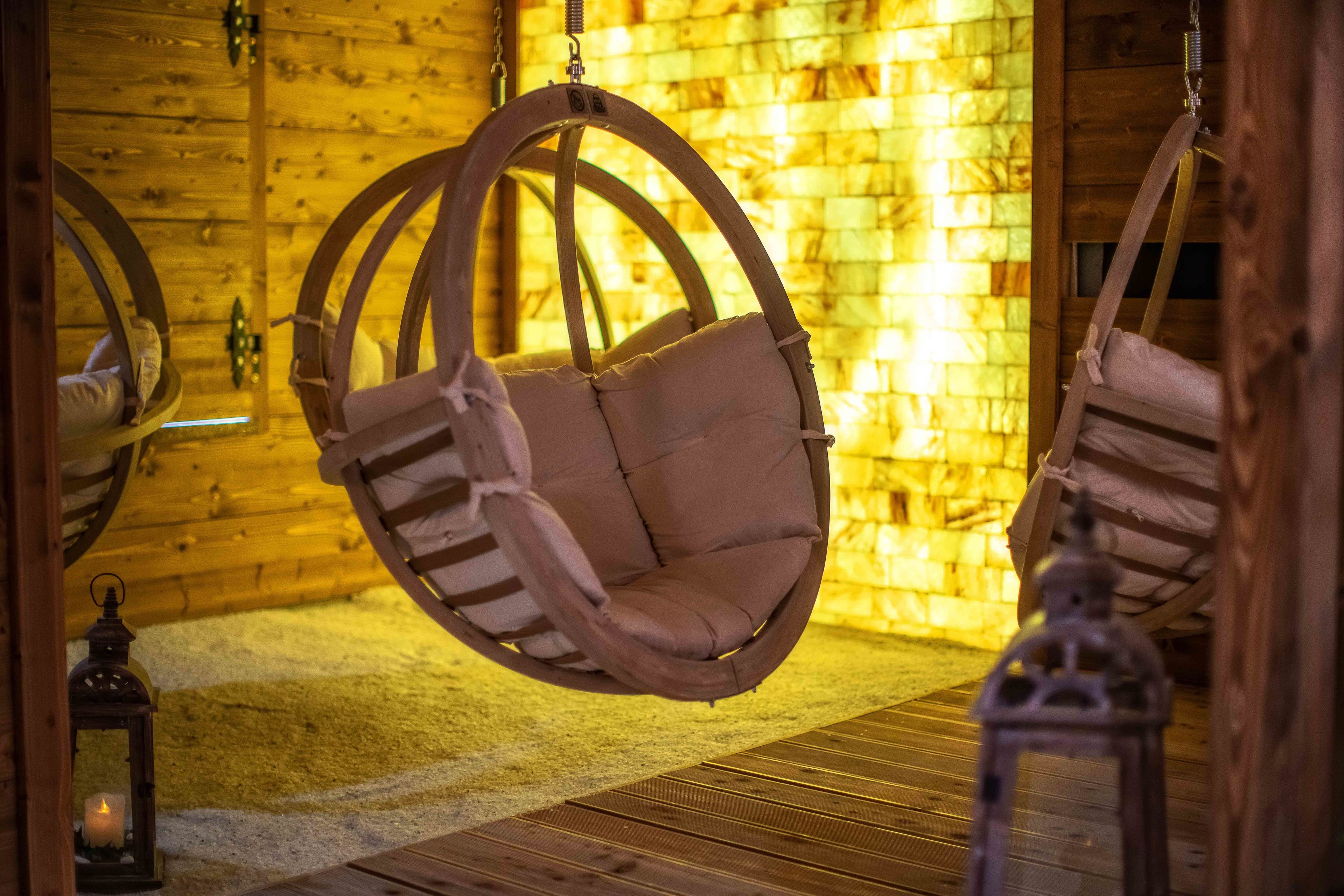 A wooden cabin interior with hanging swing chairs, a wooden floor, and a brick wall.