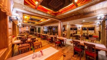 A spacious restaurant with wooden tables and chairs, a fireplace, and a high ceiling with intricate designs.