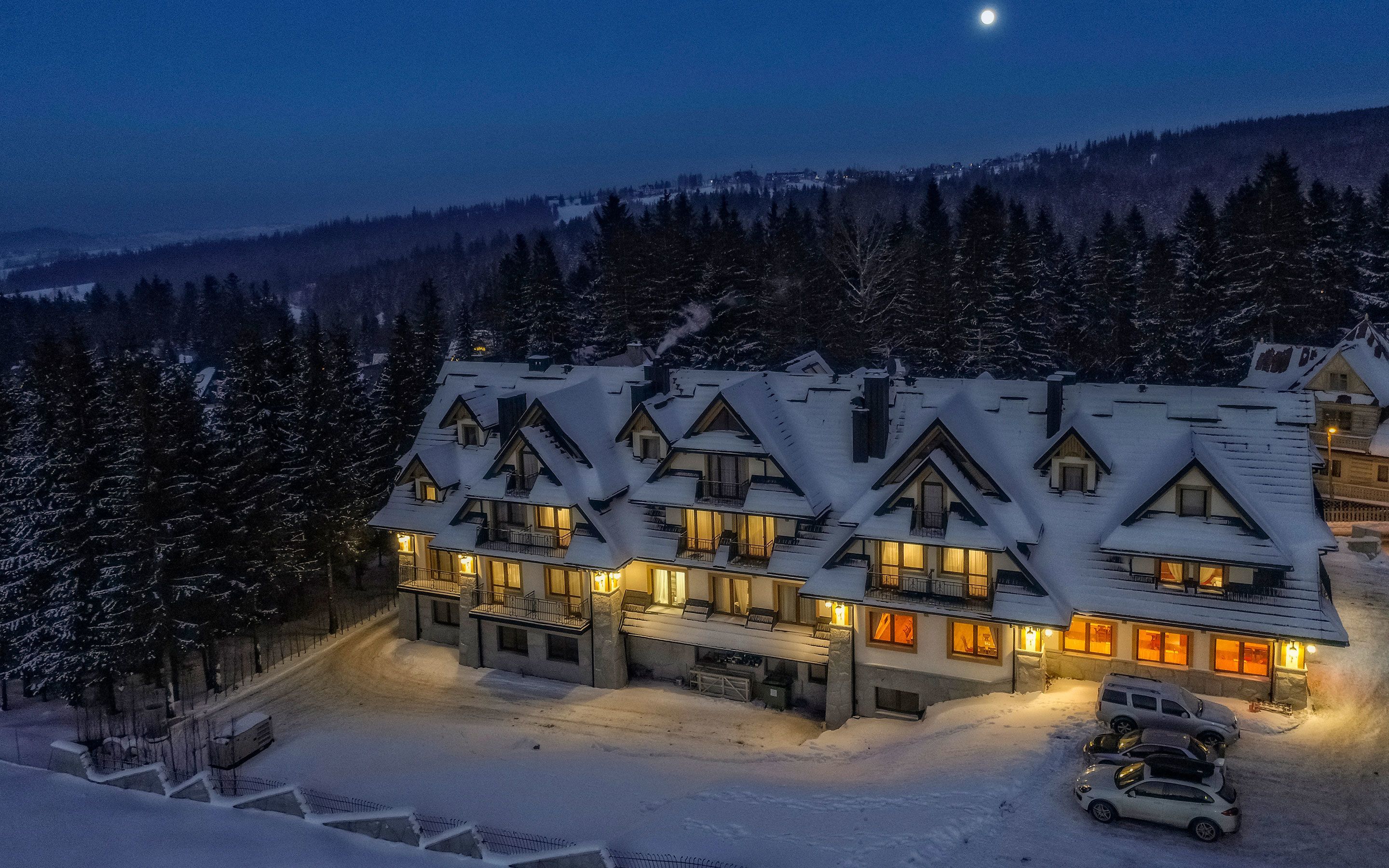 A large, multi-story lodge with a symmetrical roofline and multiple balconies, surrounded by snow-covered trees and a mountainous backdrop.