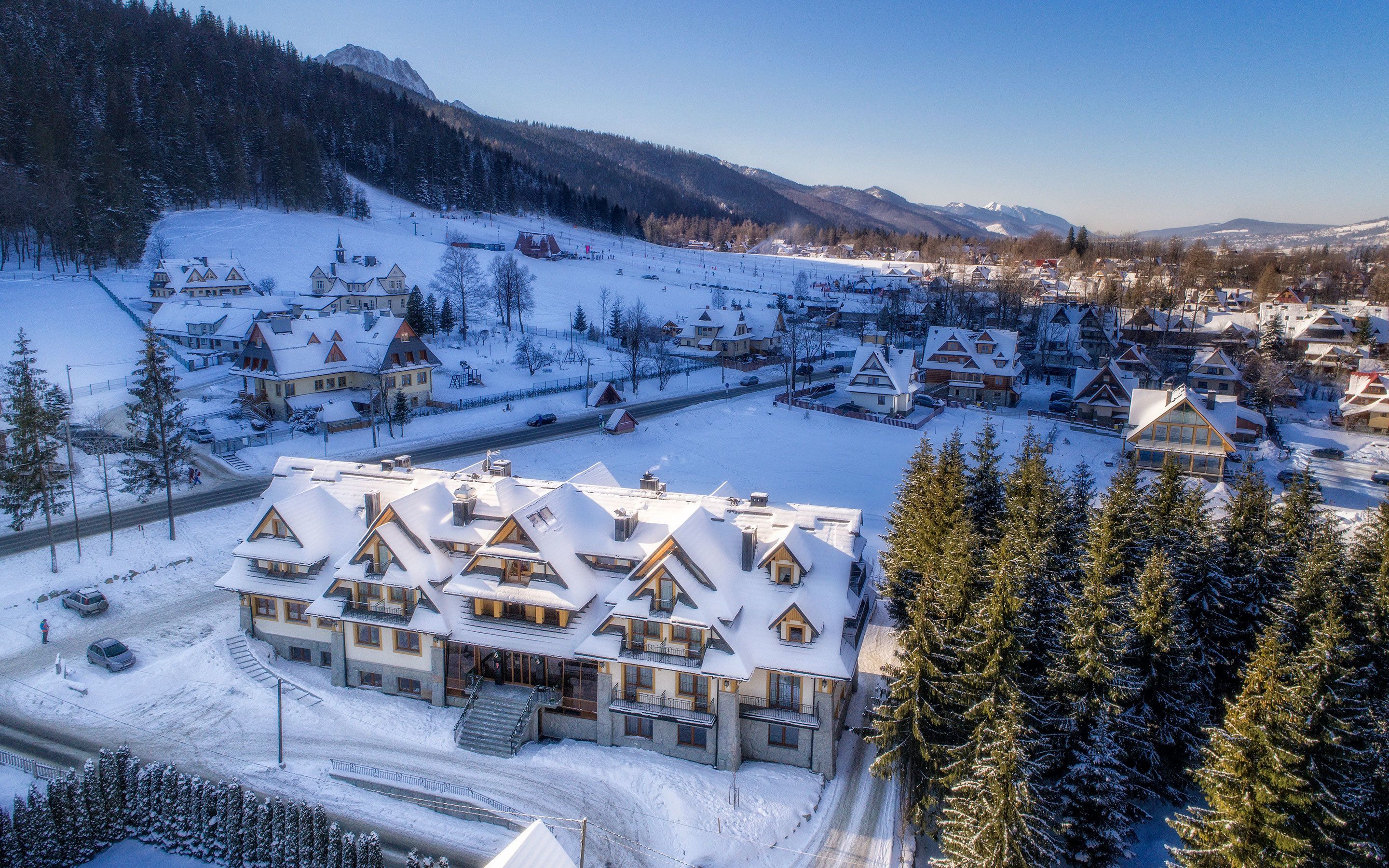 A snow-covered village with traditional wooden houses, a ski lift, and a mountain backdrop.