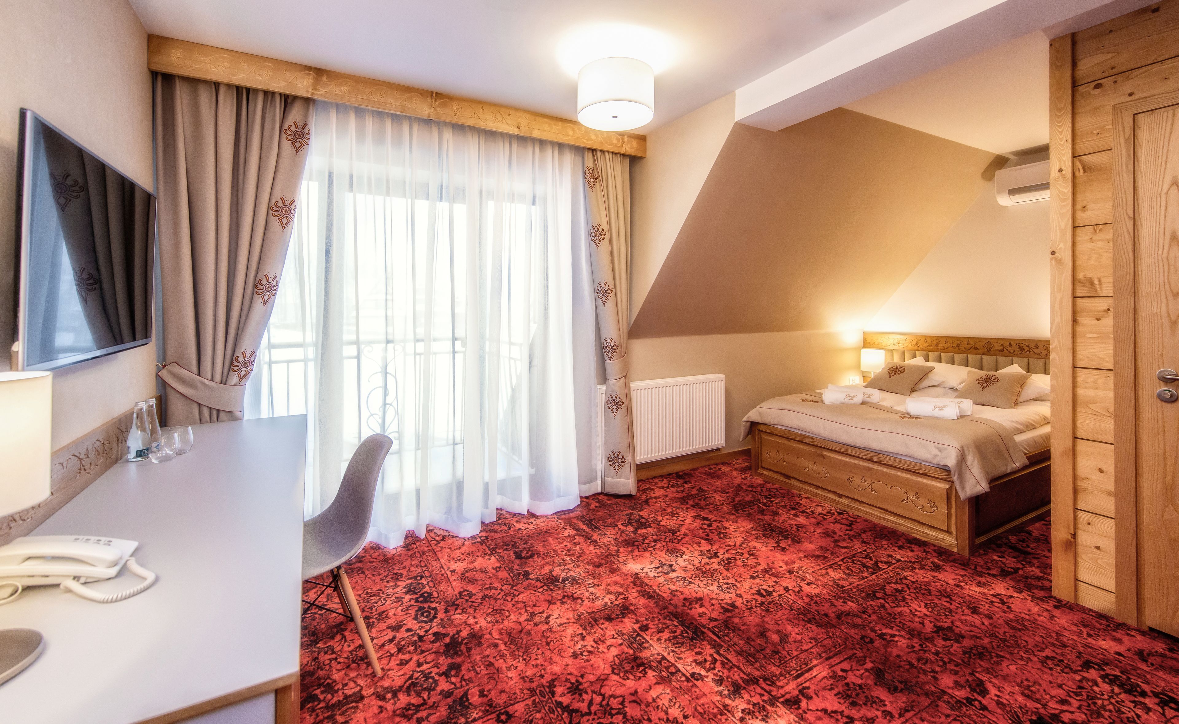 Ett hotellrum med en säng, ett skrivbord med en telefon, en stol och ett fönster med gardiner.