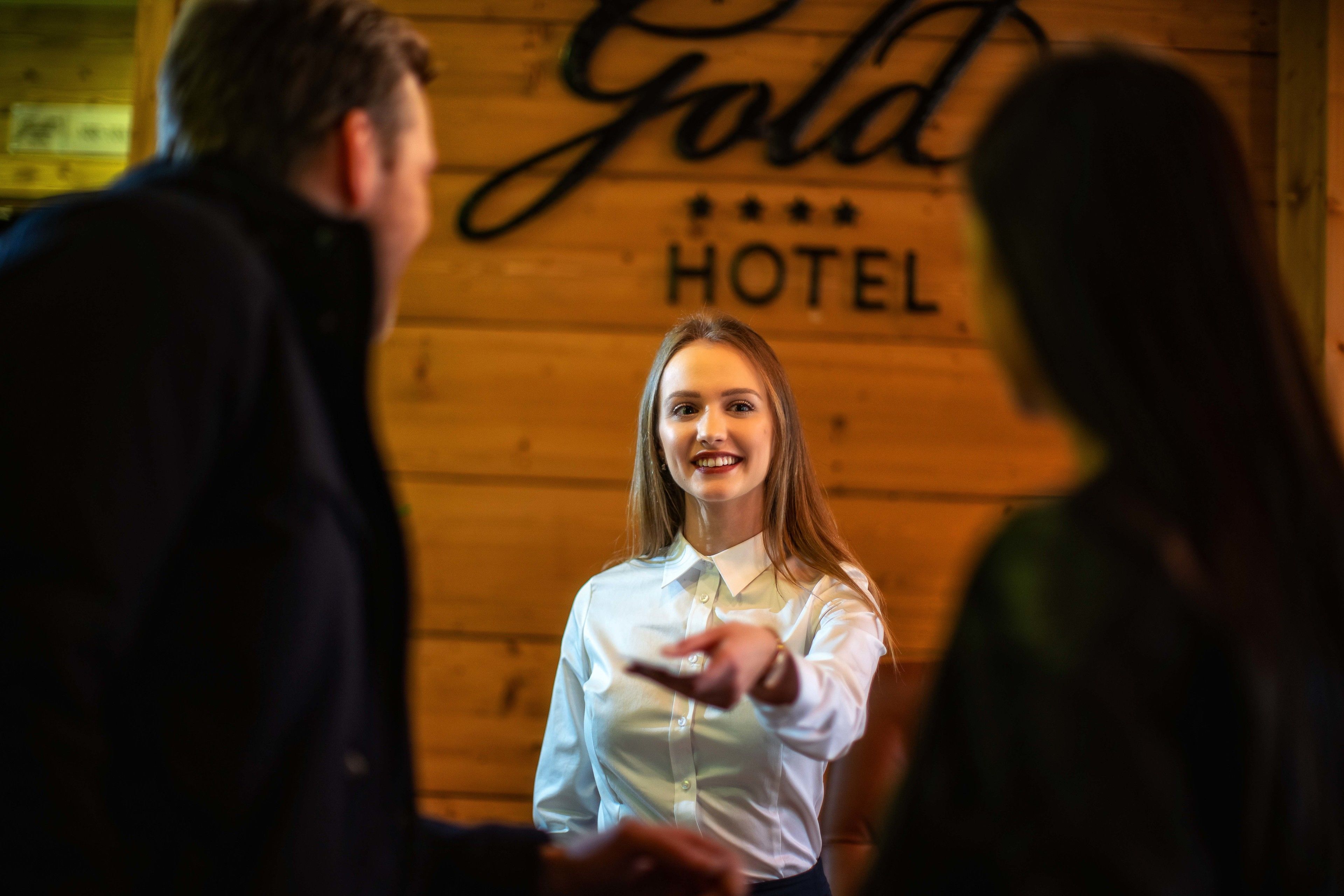 A person in a white shirt standing in front of a wooden wall with the words "Gold Hotel" visible.