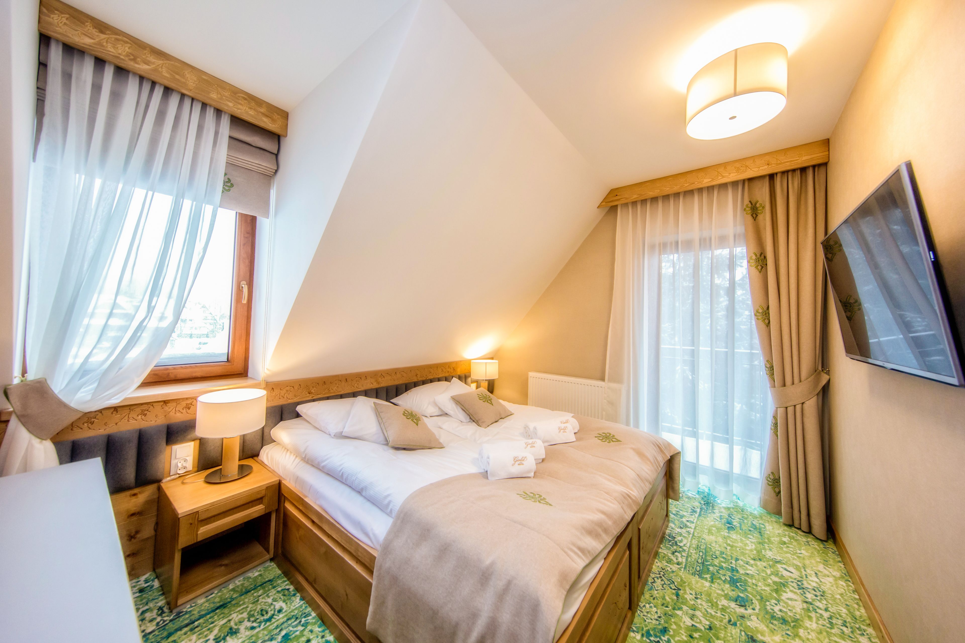 Habitación de hotel con cama, mesita de noche, lámpara, televisor y ventana con cortinas.