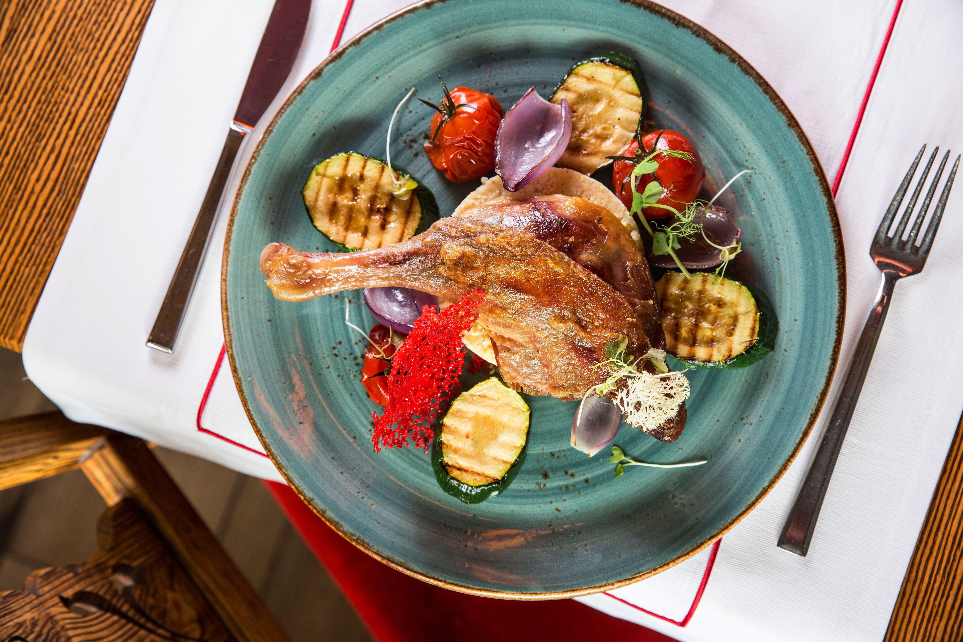A plate with grilled vegetables, a roasted duck, and some garnishes.