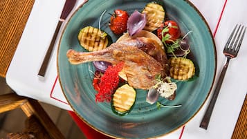 A plate with grilled vegetables, a roasted duck, and some garnishes.