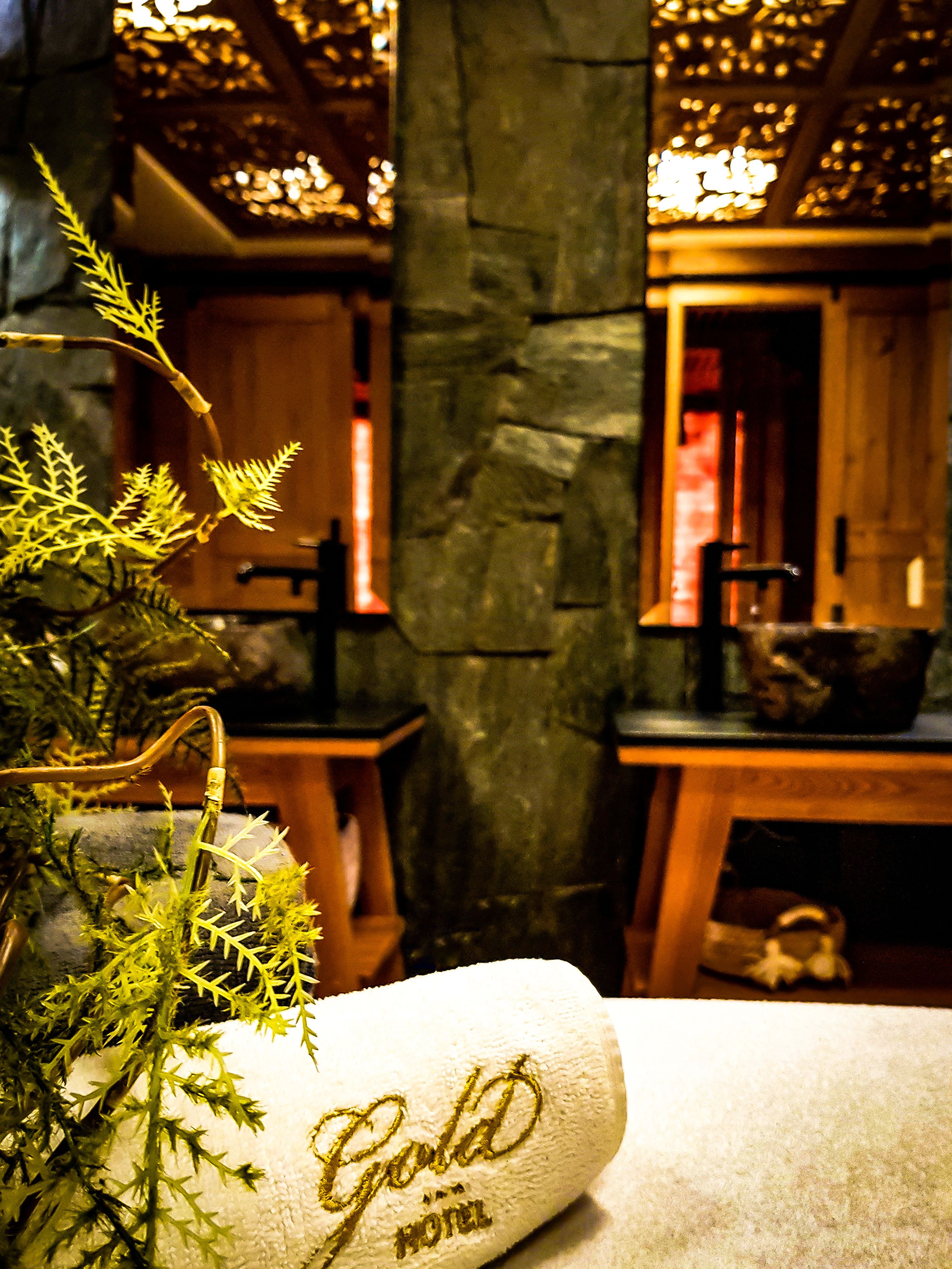 A hotel room with a stone wall, a wooden table, and a plant in a white towel.