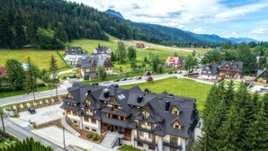 A large, multi-story building with a symmetrical roofline and multiple balconies, surrounded by lush greenery and a mountainous backdrop. - Gold Hotel (Zakopane)