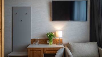 Habitación de hotel con un escritorio de madera, una silla, un televisor montado en la pared, una lámpara y un florero con flores.