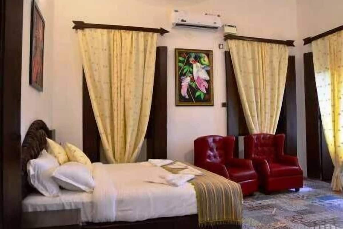 A hotel room with a bed, a red armchair, and a painting on the wall.