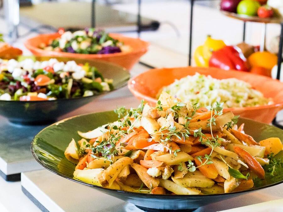 Une table de buffet proposant divers plats, notamment une salade, un plat à base de pommes de terre et un plat de légumes.