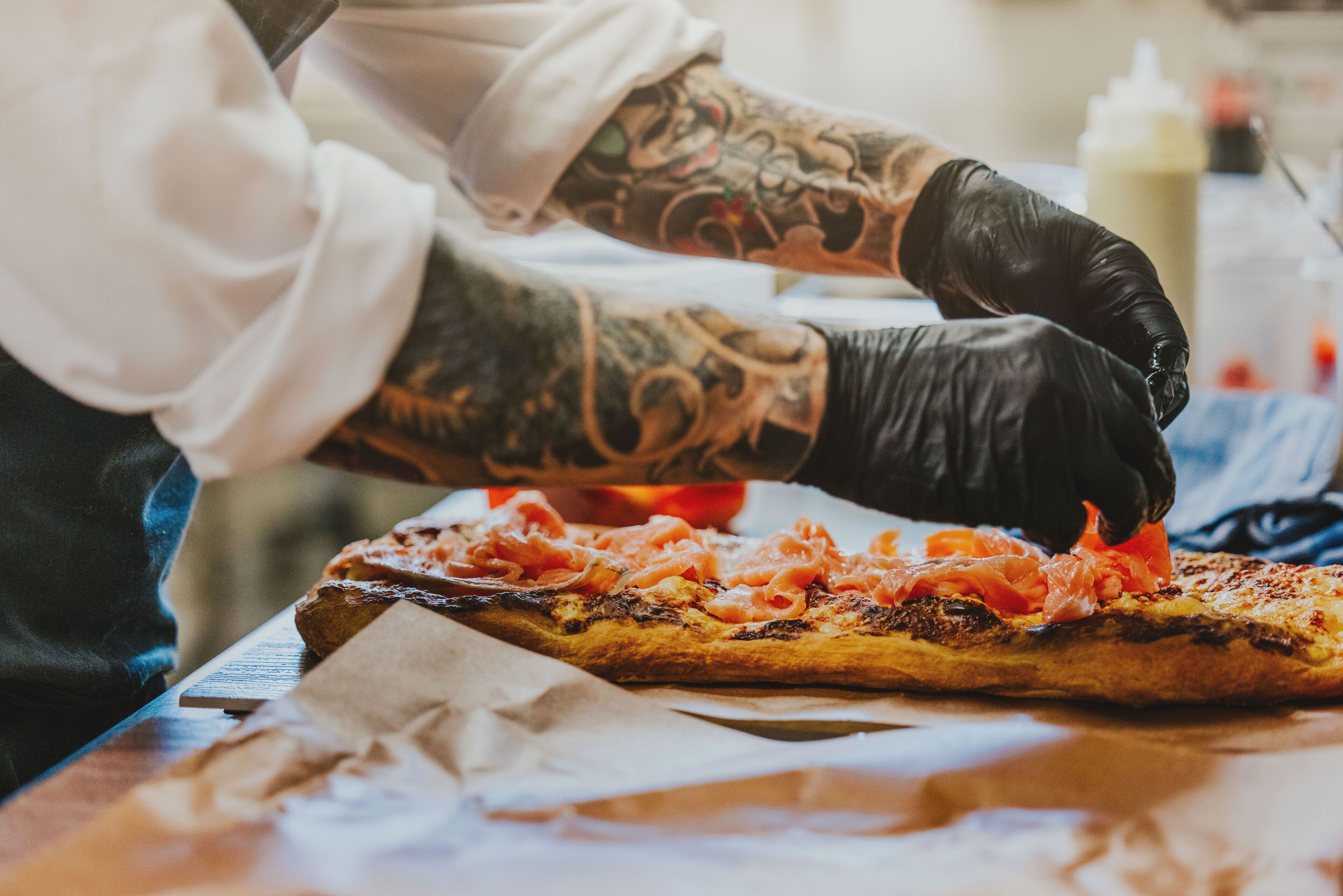 A person preparing a pizza with toppings on a wooden table.