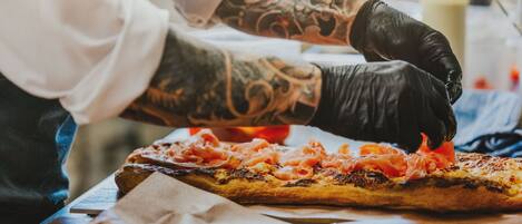 A person preparing a pizza with toppings on a wooden table.