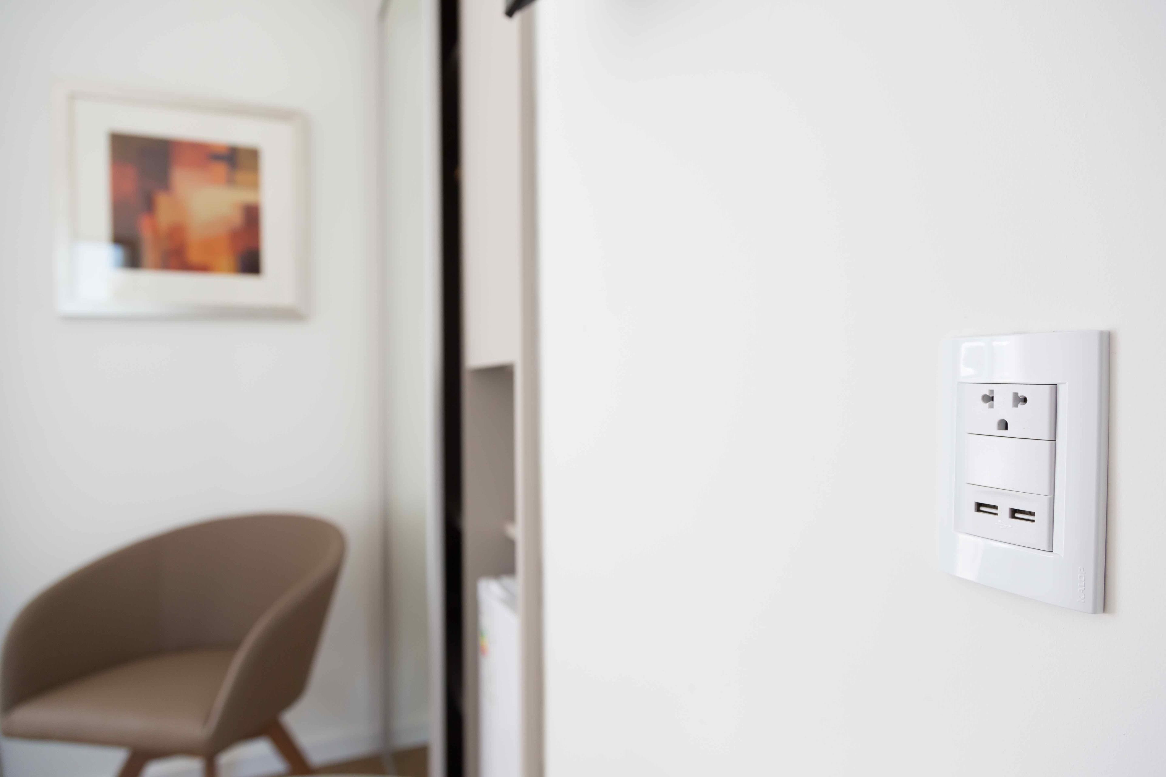 Une pièce moderne avec un mur blanc, un tableau encadré, une chaise et une prise électrique fixée au mur.