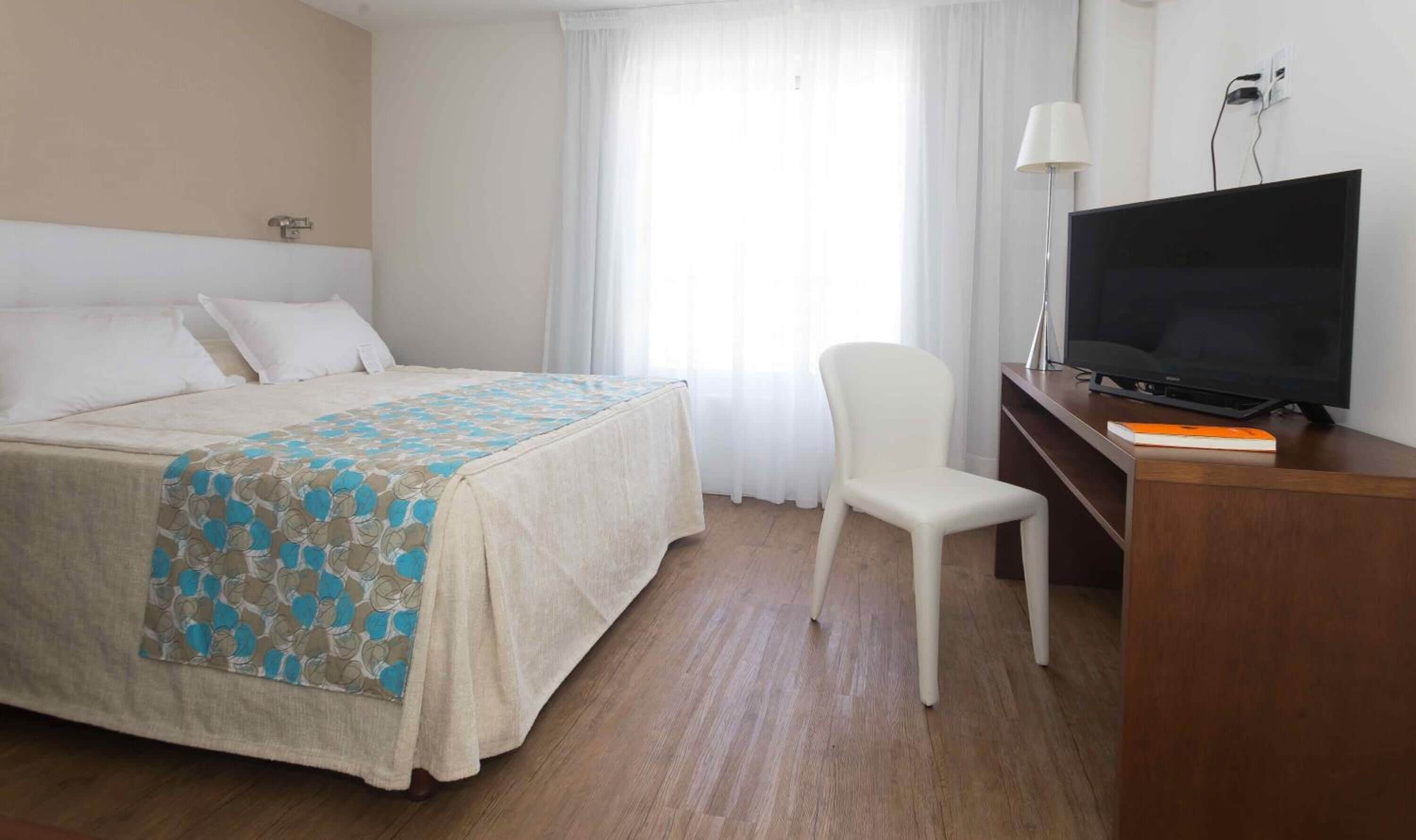 Una habitación de hotel con cama, escritorio, televisor, una silla y una lámpara.