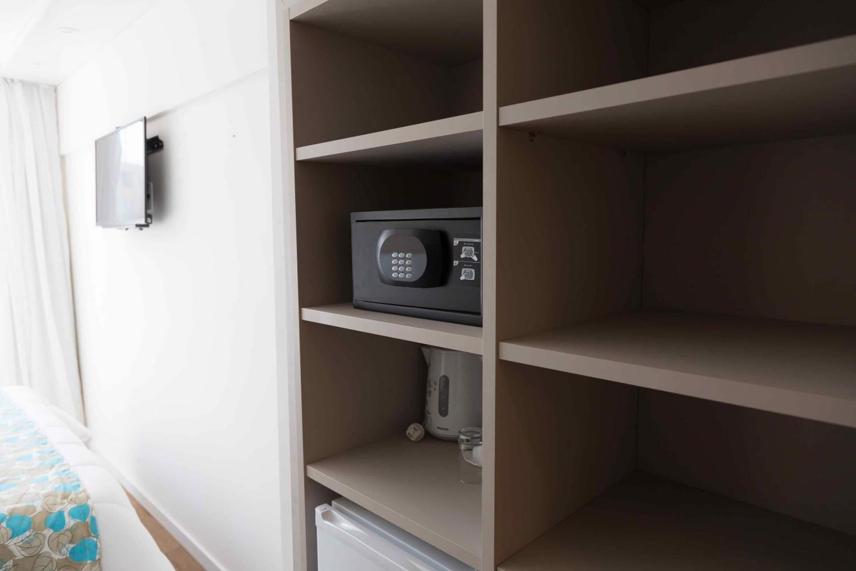A hotel room with a minibar, a microwave, and a kettle on the shelves.