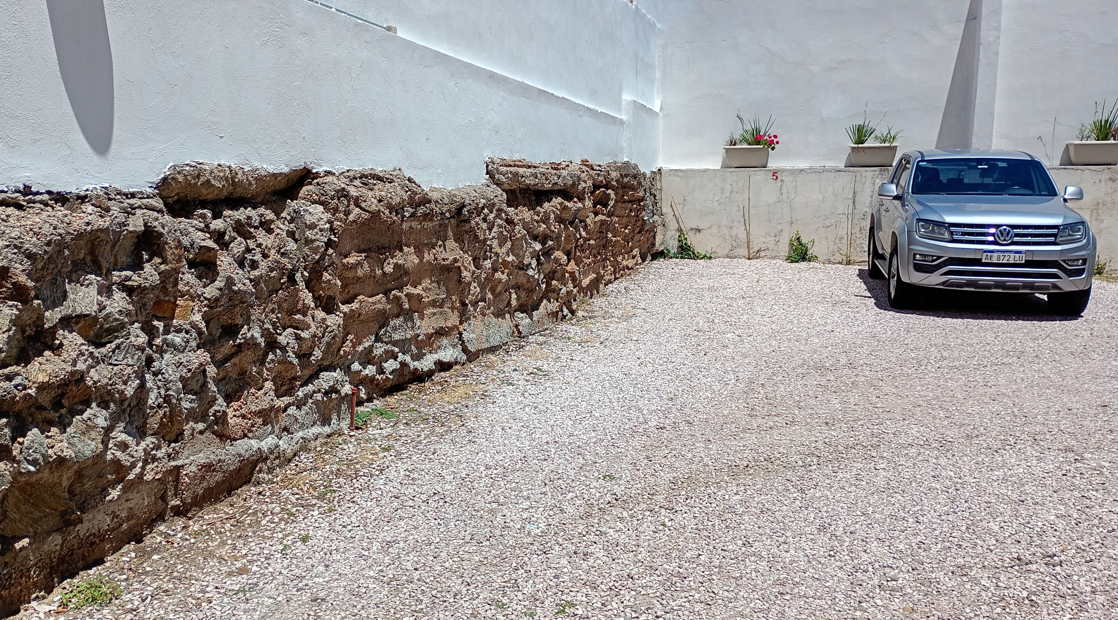 A gravel driveway leading to a building with a white wall and a Volkswagen car parked in the driveway.
