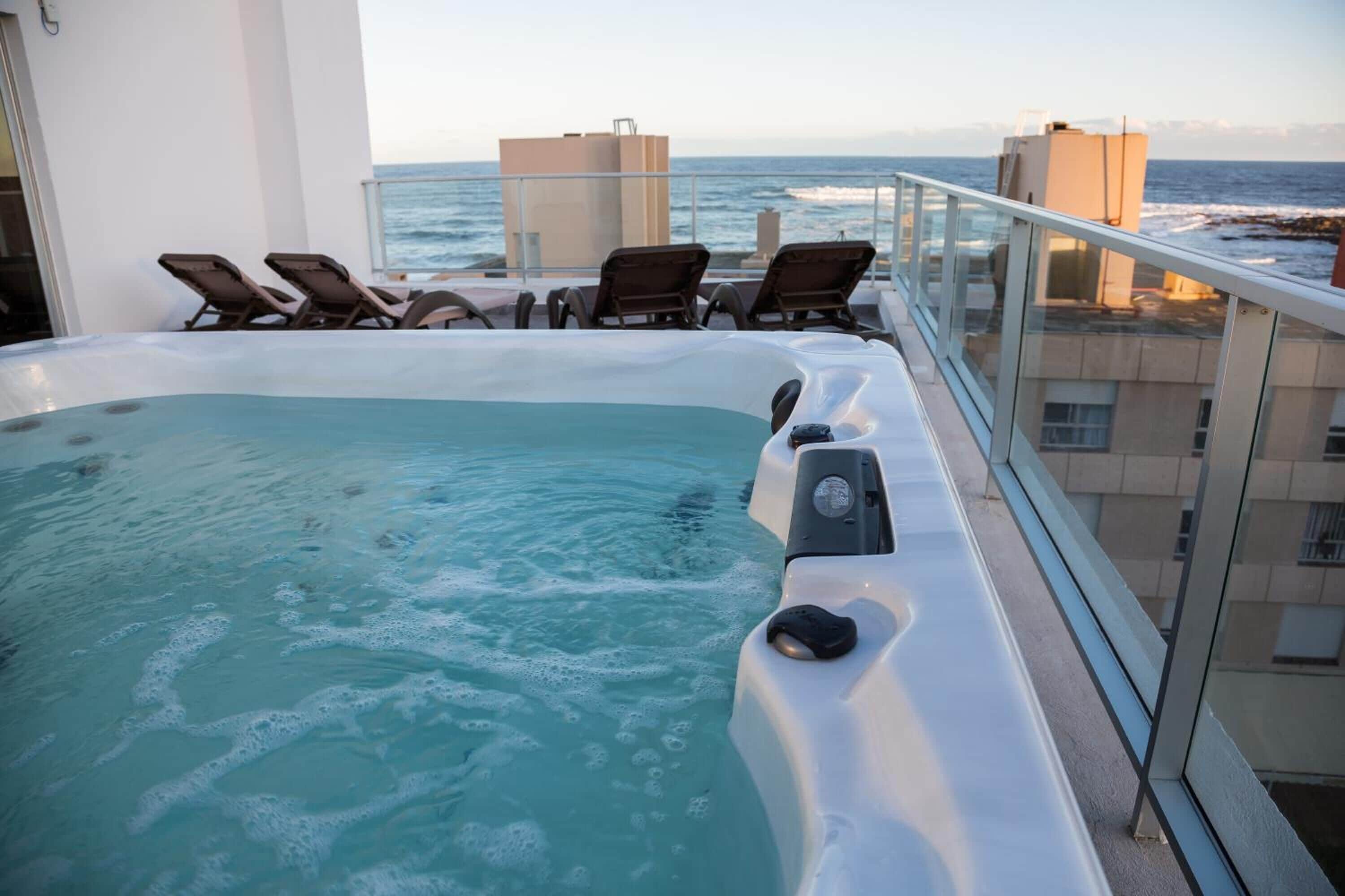 Ein Whirlpool auf einem Balkon mit Meerblick, ausgestattet mit einer Steuerung und umgeben von Liegestühlen.