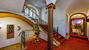Un magnifique escalier, décoré d’un sapin de Noël, orné de balustrades travaillées et recouvert d’un tapis rouge.