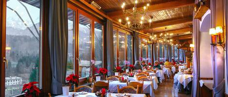 A restaurant with multiple tables set for dining, large windows, and a view of the outside.