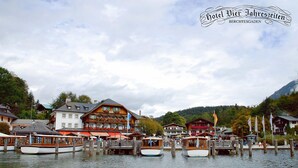 Un village au bord d’un lac, avec ses bâtiments traditionnels en bois, ses bateaux amarrés au quai et un paysage montagneux en toile de fond.
