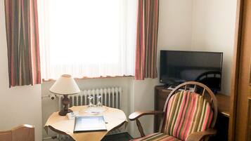Ein Hotelzimmer mit Bett, Schreibtisch mit Lampe, Stuhl, Fernseher und Vorhängen.