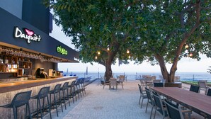 Un área de bar al aire libre con asientos, una barra y vista al mar.