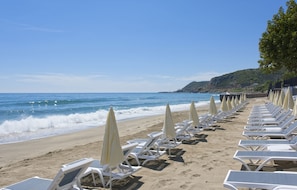 A beach with rows of white lounge chairs and yellow umbrellas, a sandy shore, and the ocean in the background. - Floria Beach Hotel (Alanya)