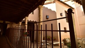 A covered outdoor area with a metal fence, potted plants, and a building with a tiled roof in the background. - Palacio Rejadorada (Toro)