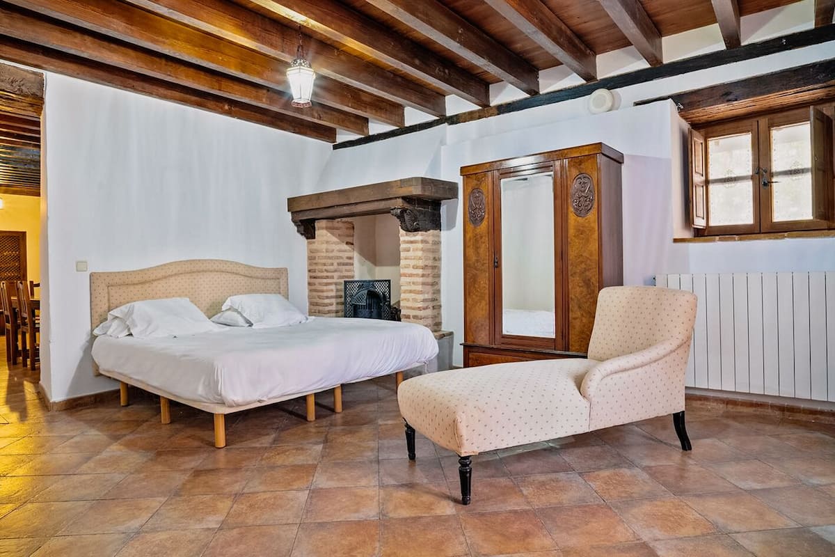 Un dormitorio con cama, una silla, un armario y una chimenea.