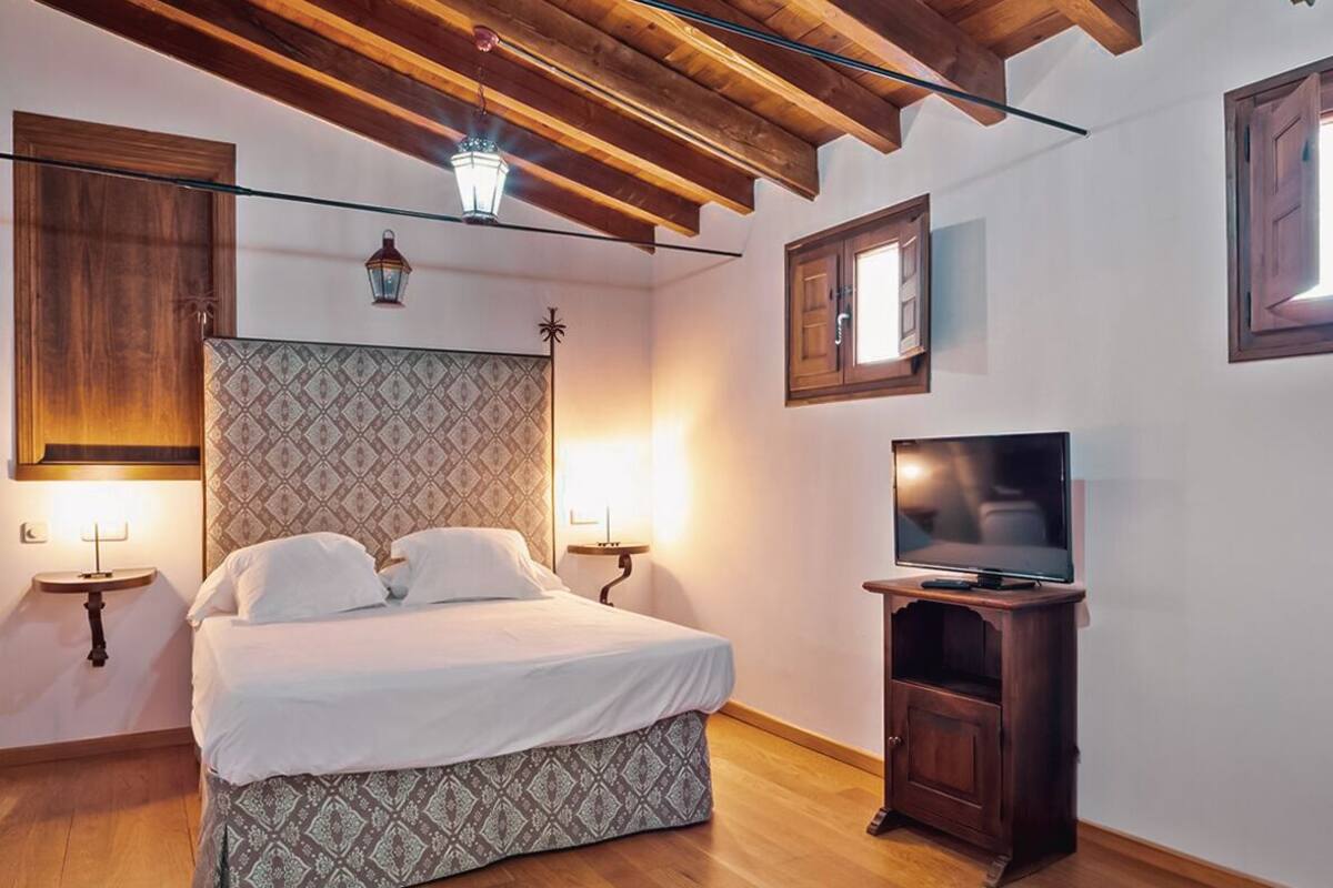 Un dormitorio con cama, lámparas de noche, televisor y techo de madera.