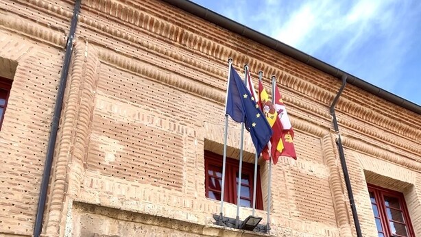 A historic building with a large wooden door and multiple flags, including the European Union flag. - Palacio Rejadorada (Toro)