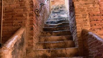 Una escalera de piedra con un muro de ladrillo a un lado y una barandilla de metal al otro, que conduce a un arco de entrada.