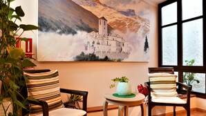 Ein Zimmer mit zwei Stühlen, einem kleinen Tisch und einem Gemälde von einer Berglandschaft.