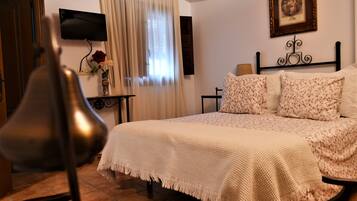 Un dormitorio con cama, televisor montado en la pared, una mesita con un jarrón de flores y una silla.