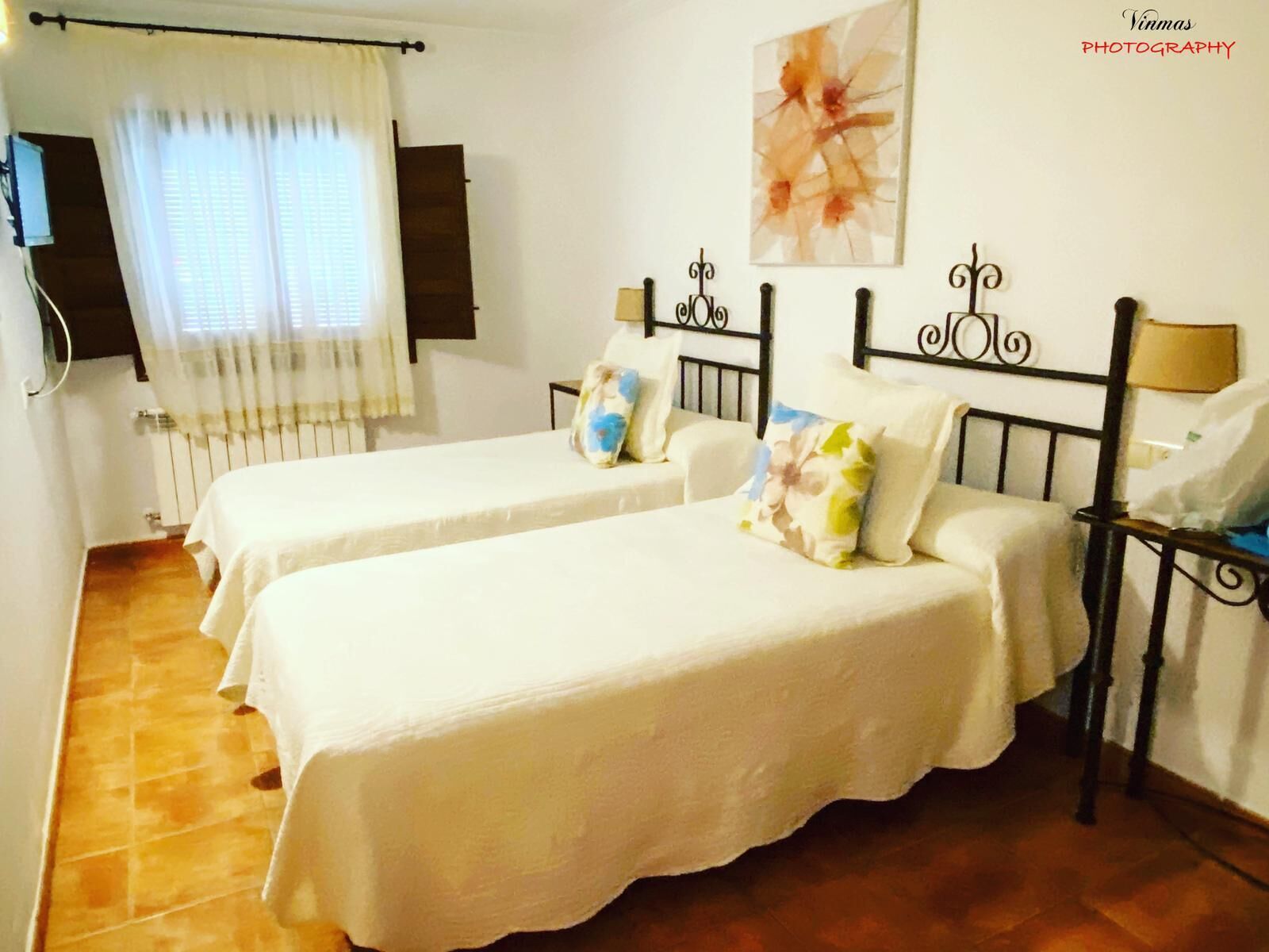 Una habitación con dos camas individuales, un radiador, una ventana con cortinas y una obra de arte colgada en la pared.