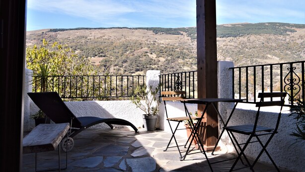 Ein Balkon mit Steinboden, einem schwarzen Liegestuhl, einem Holztisch und einem Blumentopf.