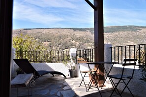 A balcony with a stone floor, a black lounge chair, a wooden table, and a potted plant. - Hotel Rural Alfajía de Antonio (Capileira)