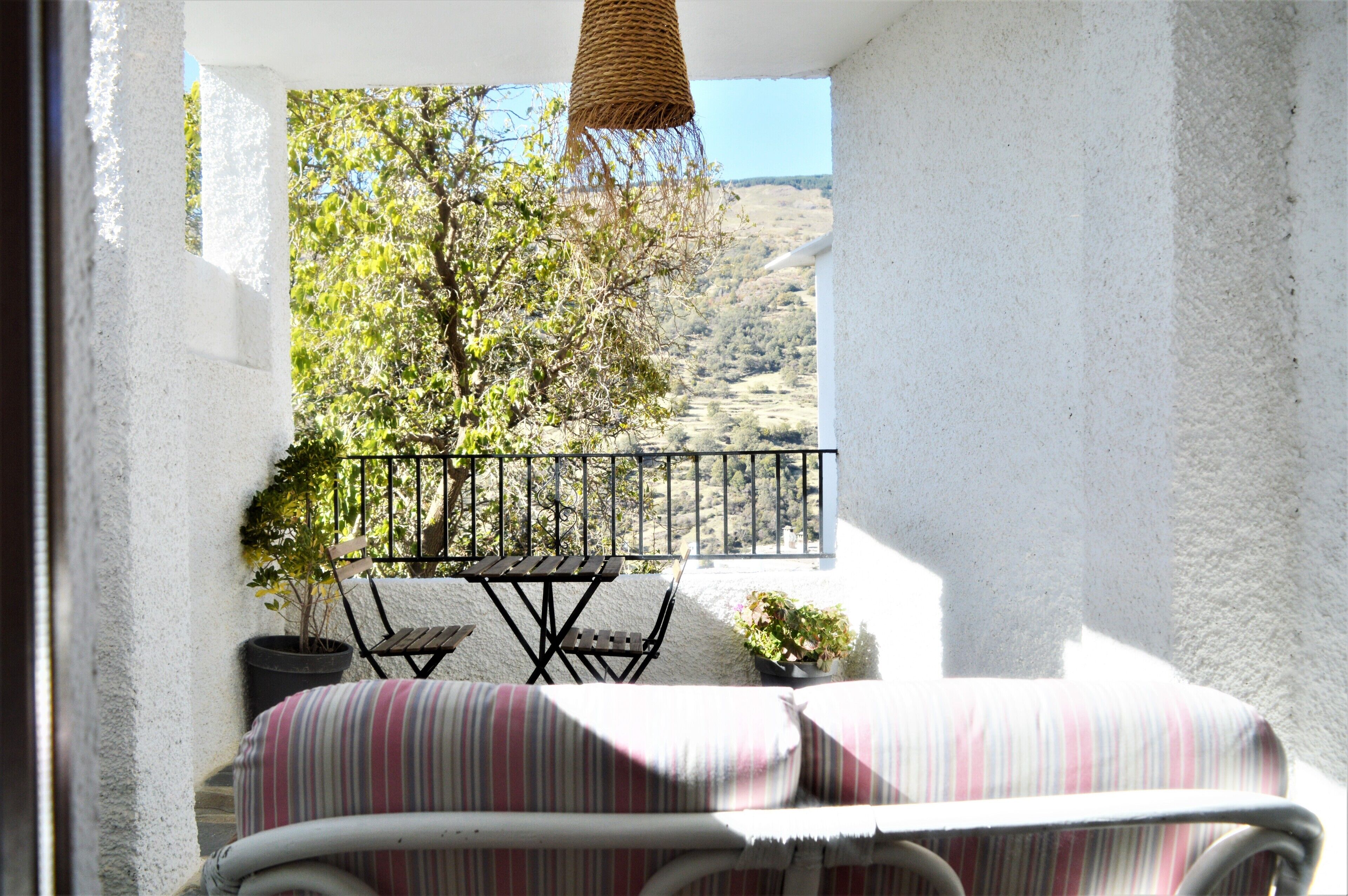 A balcony with a table and chairs, a hanging basket, and a potted plant.