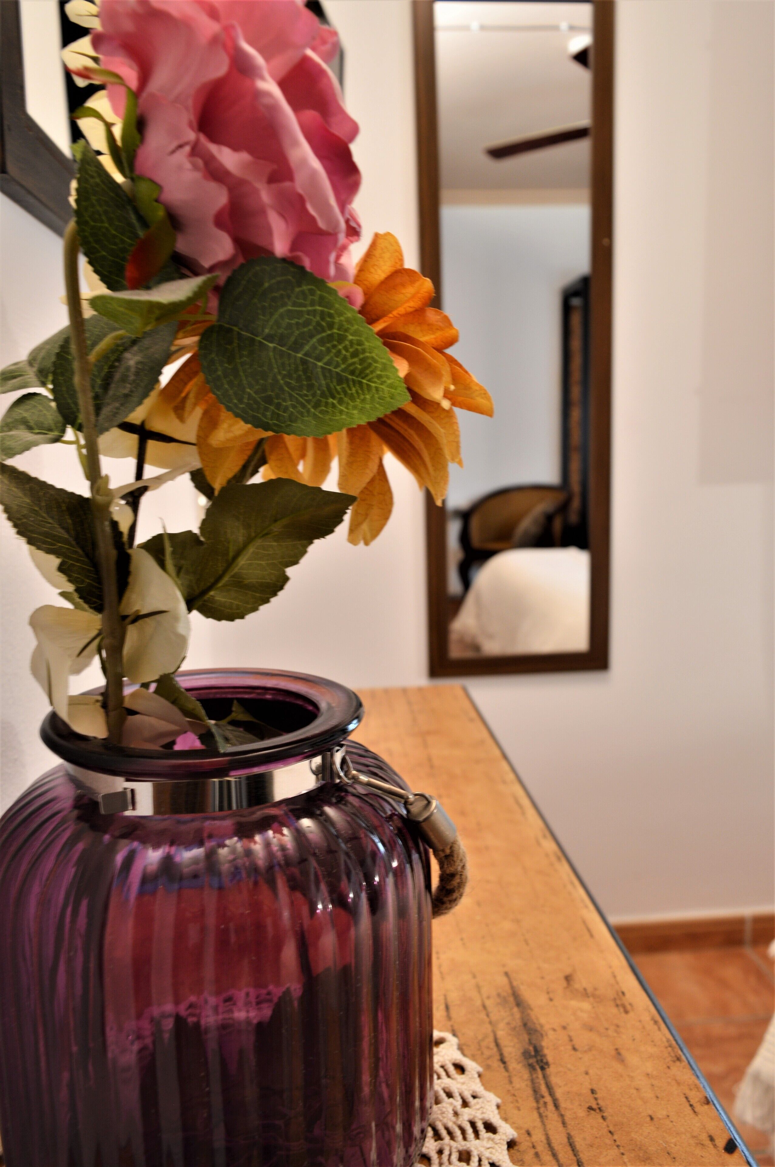Un jarrón morado con un arreglo floral sobre una mesa de madera.