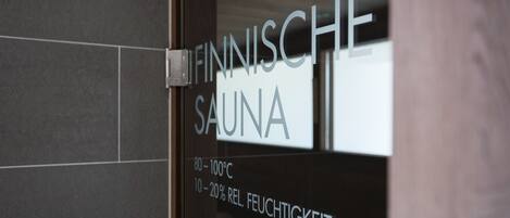 Una puerta de cristal con el texto "FINNISCHE SAUNA" e indicaciones de temperatura "80-100°C" y "10-20% REL. FEUCHTIGKEIT".