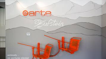A wall with the text "arte Bufstein" and two orange chairs.