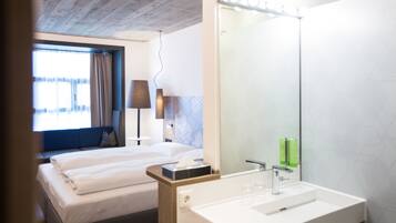 A hotel room with a bed, a bathroom with a sink and mirror, and a window with curtains.