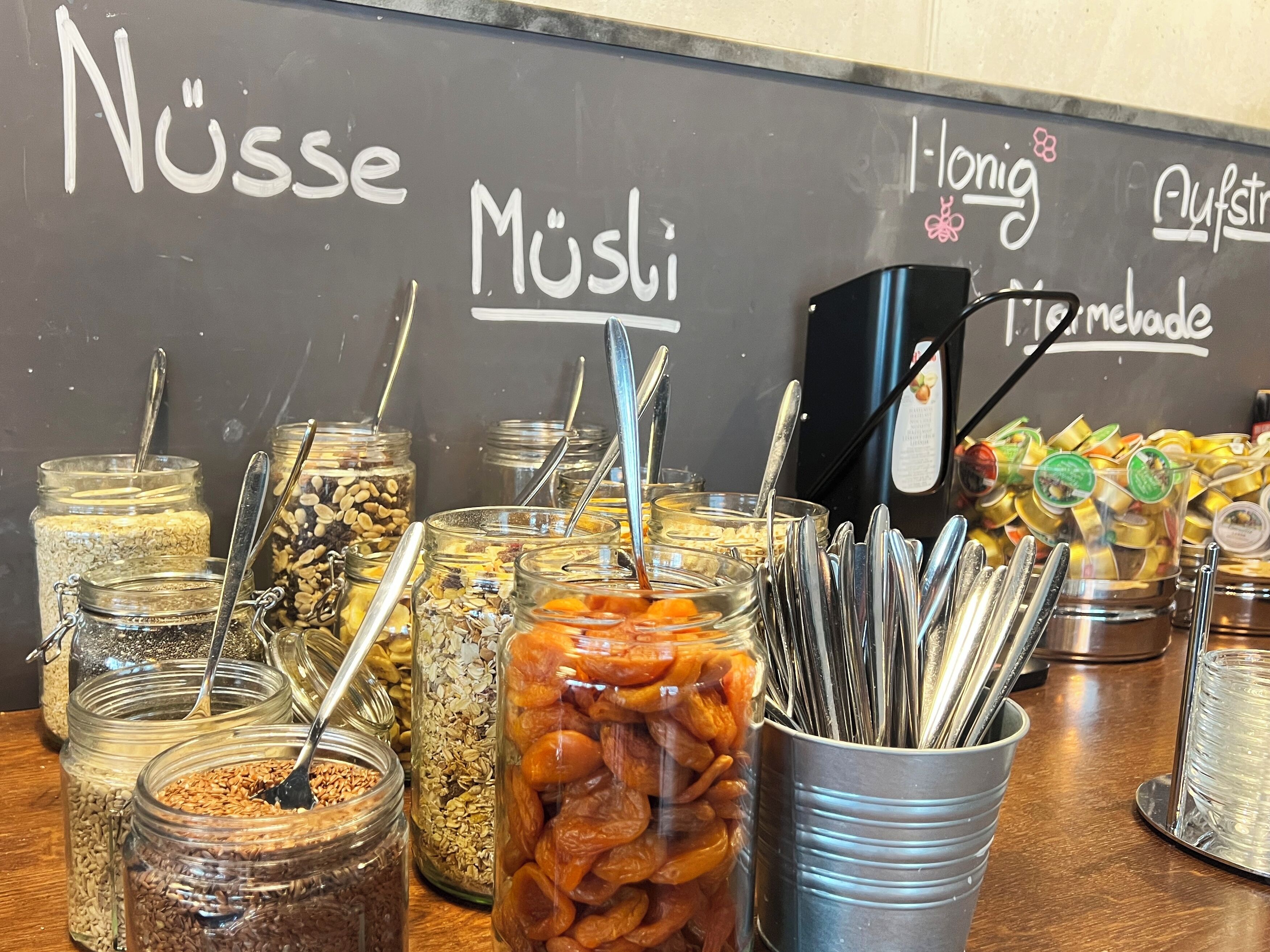 Diversos alimentos en frascos y recipientes, con utensilios, y una pizarra con texto al fondo.