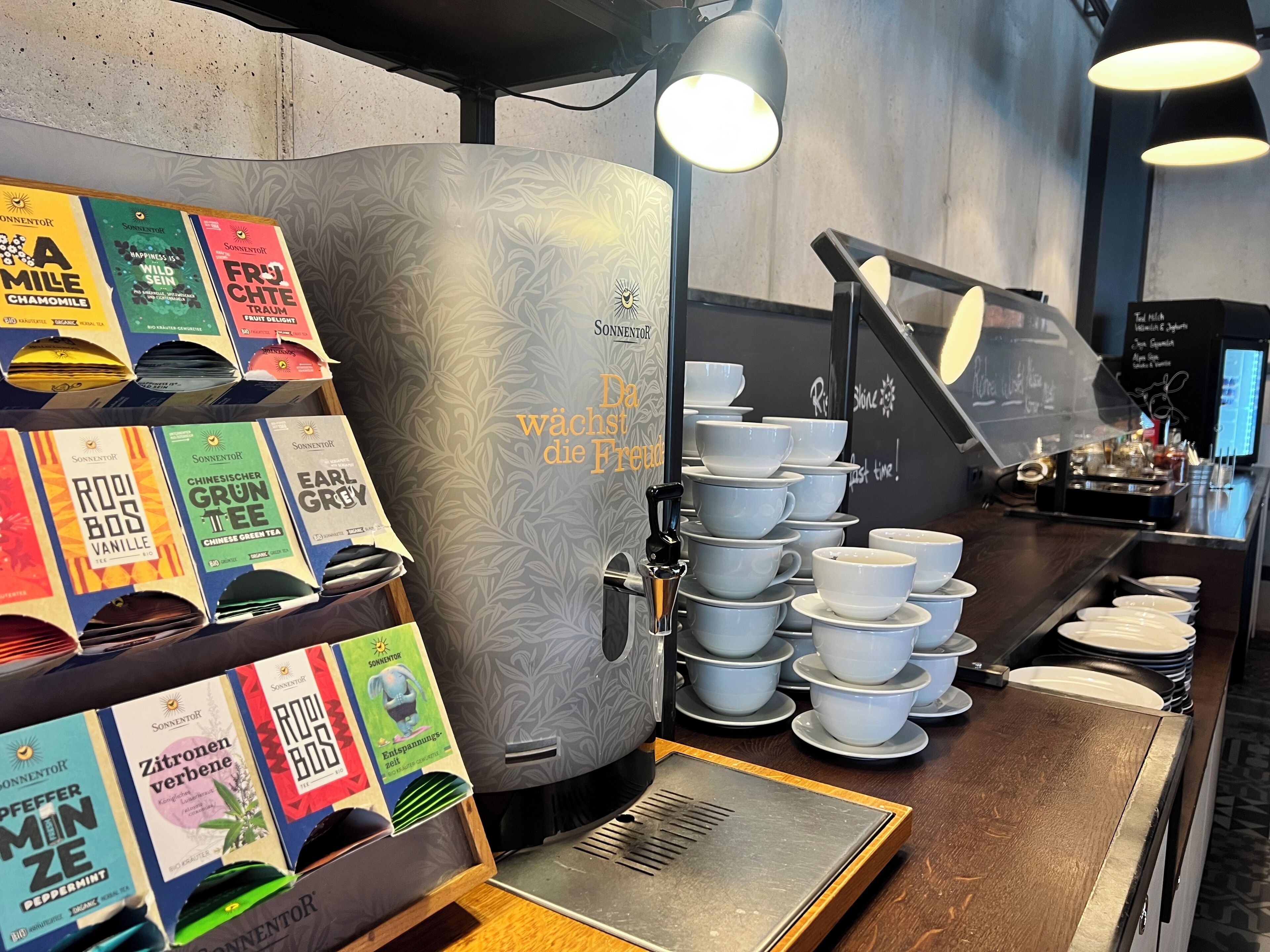 A coffee shop interior with a coffee machine, tea dispensers, and a menu board.
