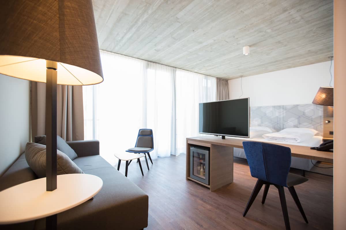 Ein modernes Hotelzimmer mit einer Couch, einem kleinen Tisch, einem Schreibtisch mit Fernseher und einem Sessel.