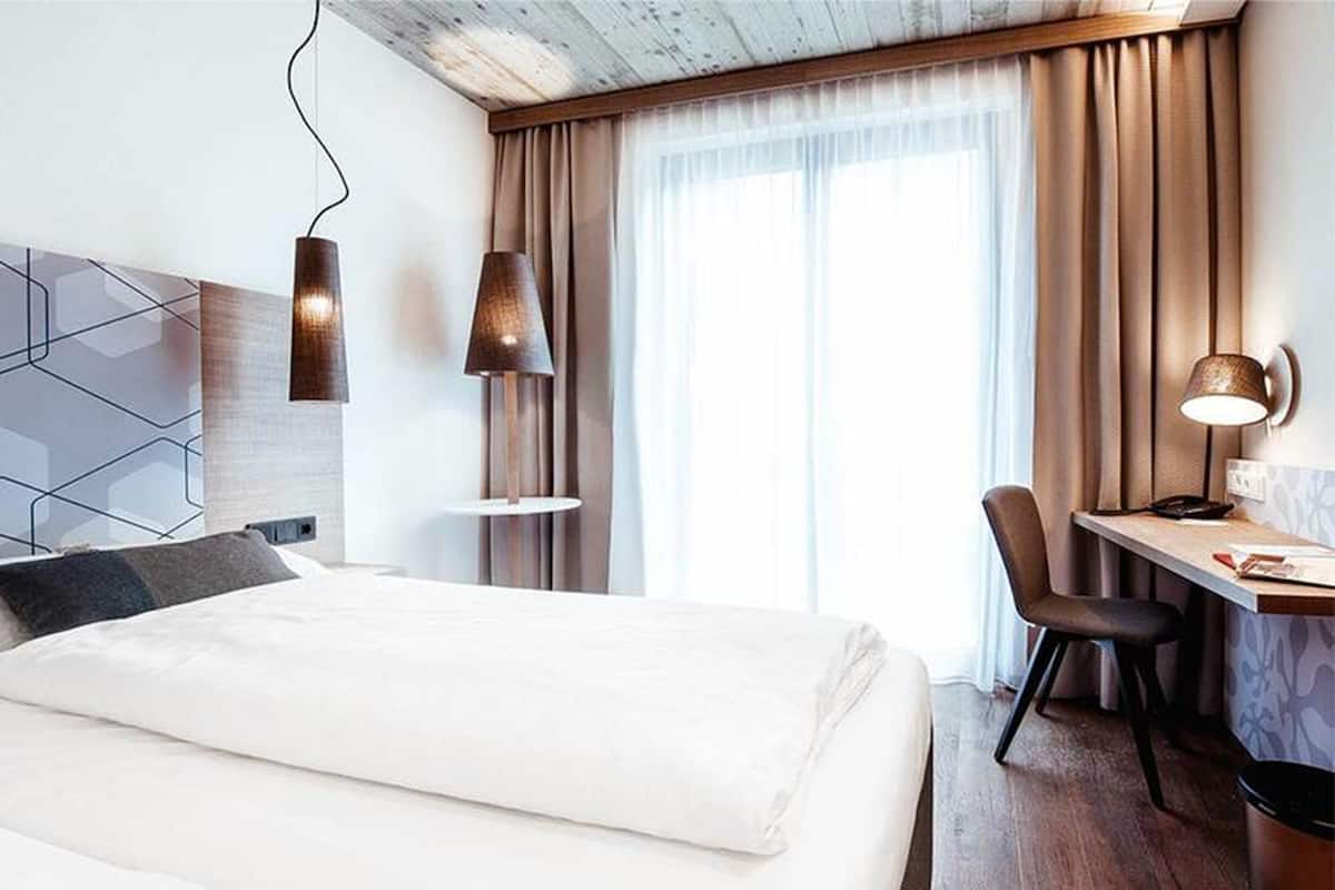 Ein Hotelzimmer mit Bett, Schreibtisch, Stuhl und zwei Wandlampen.