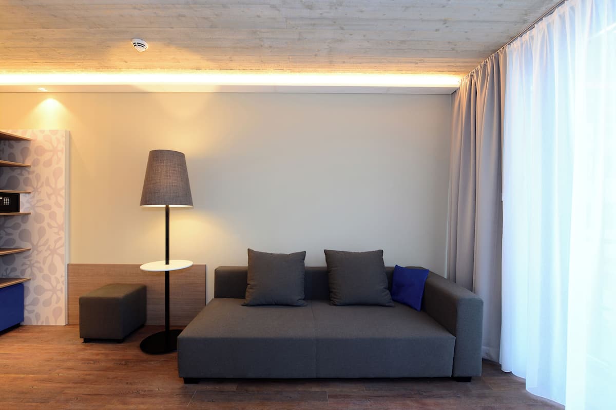 Ein modernes Wohnzimmer mit einem grauen Sofa, einer Stehlampe und einem kleinen Hocker.