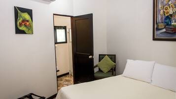 Un dormitorio con cama, una silla con almohada, una puerta y un cuadro colgado en la pared.
