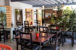 A restaurant with wooden tables and chairs, potted plants, and artwork on the walls.
